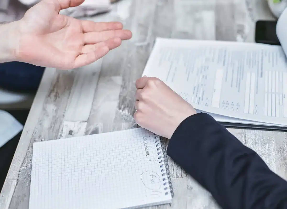 Schreibtisch mit Antragsformularen, Dokumenten und Ordnern, eine Hand mit Stift beim Unterzeichnen