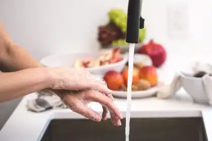 Hände unter kaltem fließendem Wasser an einem Waschbecken, Seifenschaum sichtbar.