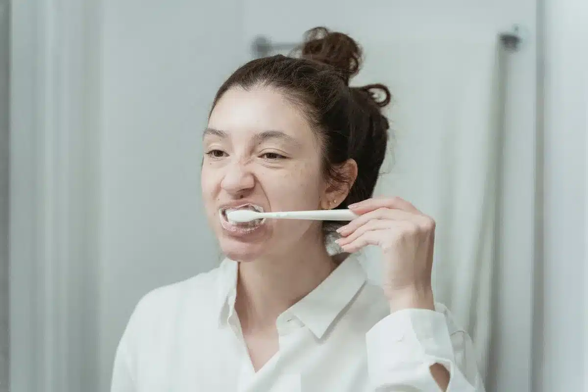 Jugendlicher putzt sich die Zähne morgens im Badezimmer mit fluoridhaltiger Zahnpasta